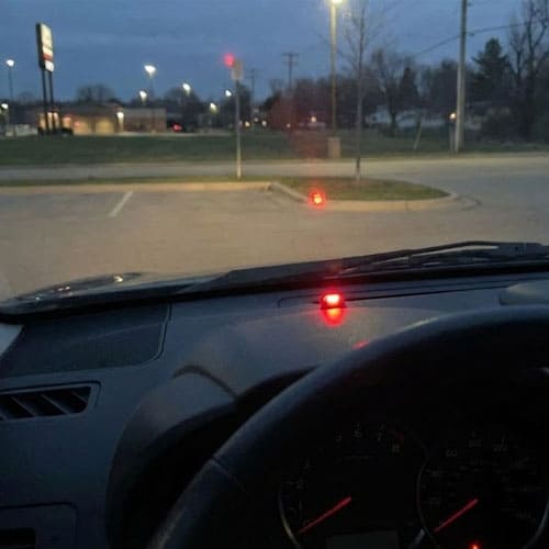 Вид из салона автомобиля в сумерках: мигает красная лампочка индикатора иммобилайзера под лобовым стеклом