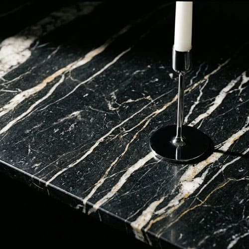 Крупный план слэба чёрного мрамора Nero Marquina с золотыми прожилками и тонким хромированным подсвечником
